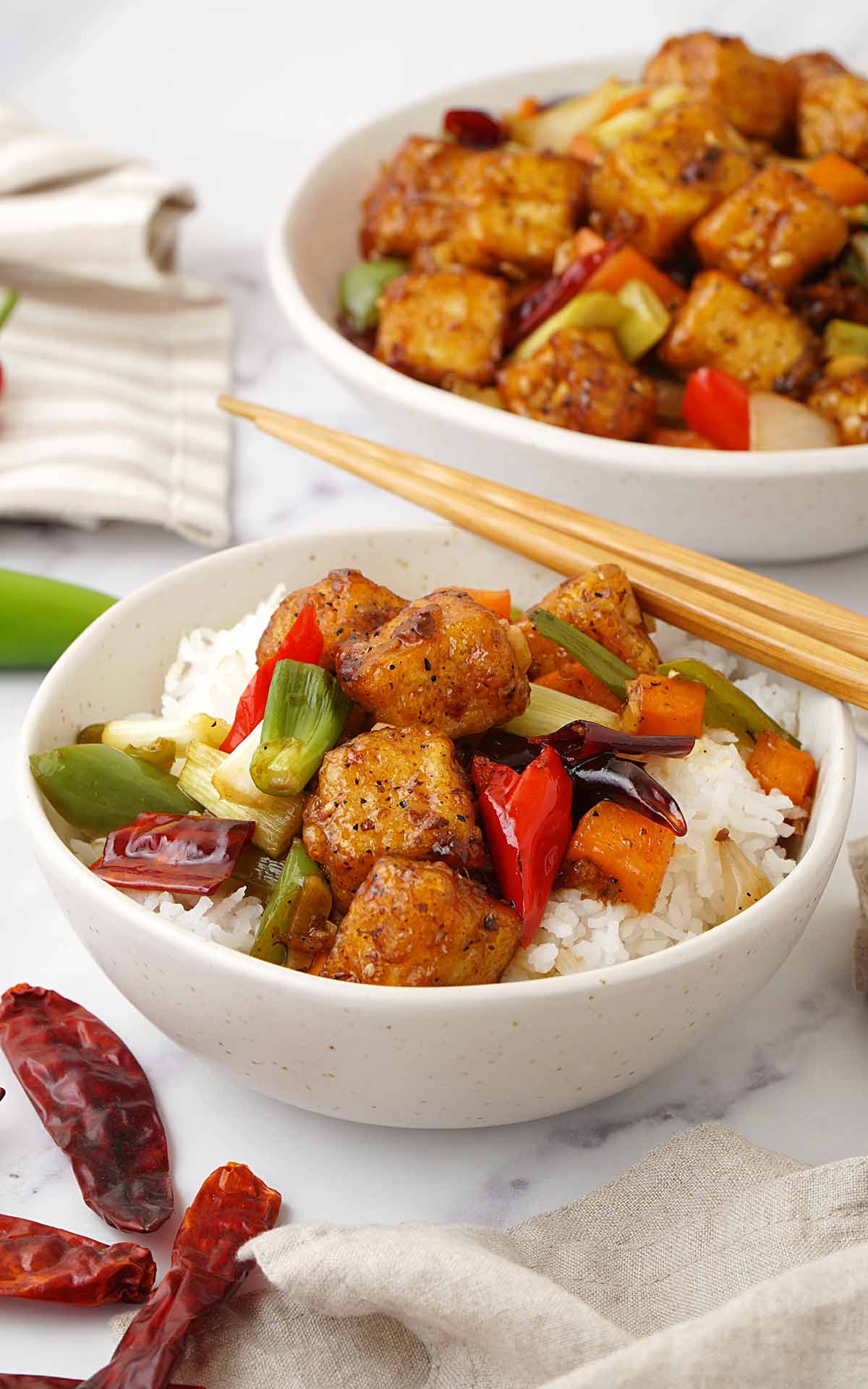 A white bowl containing, Szechuan tofu stir fry carrots, chilli peppers, and spring onions. 