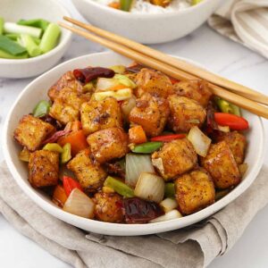 A white bowl containing, fried golden tofu cubes with vegetables in spicy Szechuan sauce.