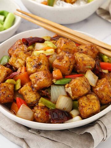 A white bowl containing, fried golden tofu cubes with vegetables in spicy Szechuan sauce.
