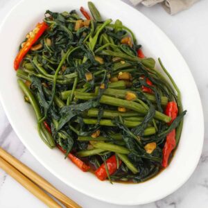 A white oval plate containing, stir fried morning glory with Thai red chillies and garlic.