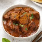 A white bowl containing, lamb tikka with masala curry sauce and coriander.