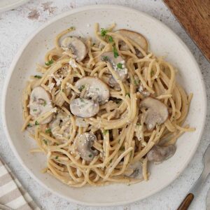 A white plate containing spaghetti with mushroom and cream sauce.