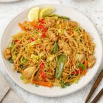 A white plate containing Filipino Pancit Bihon with chicken and vegetables.