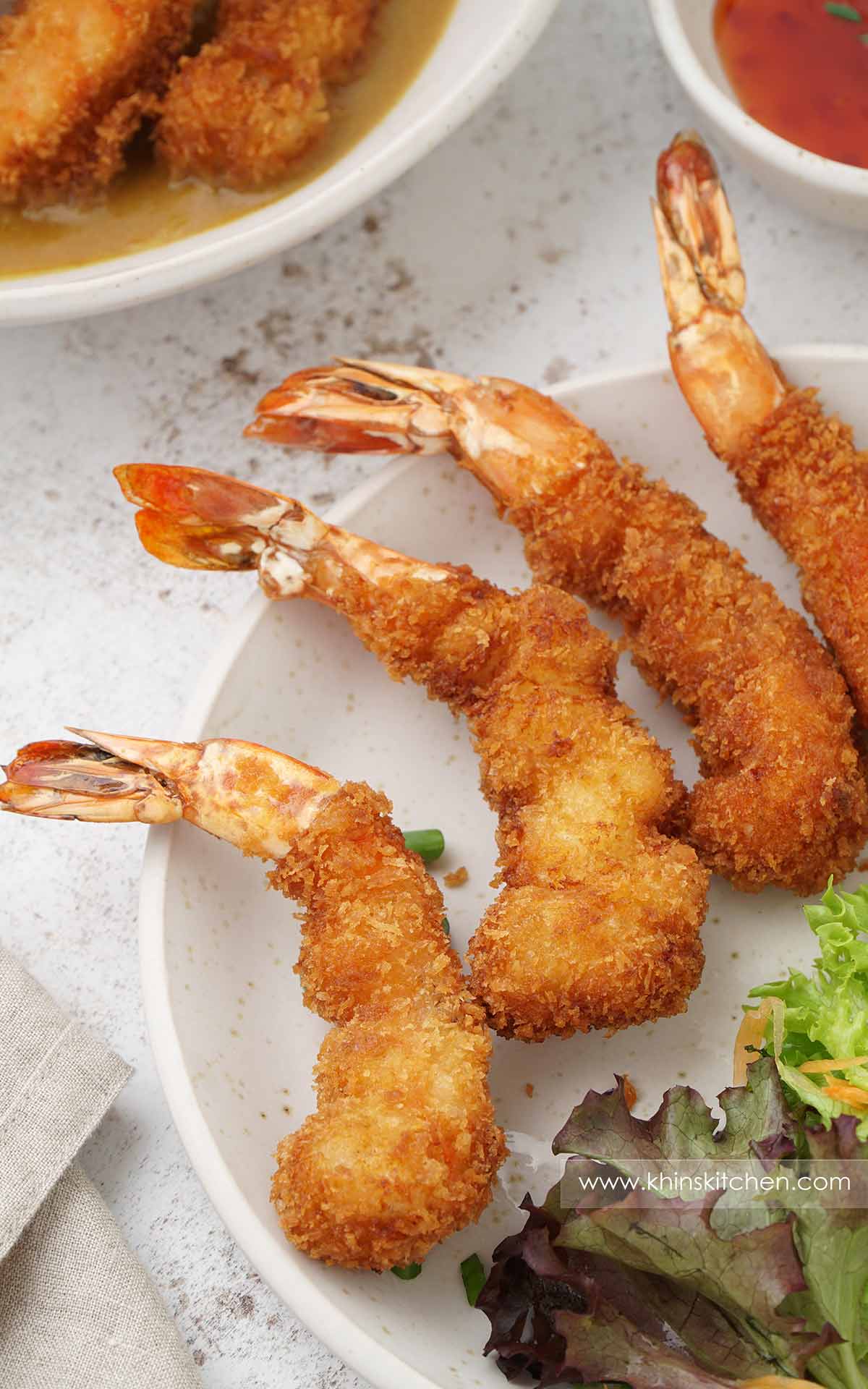 A white plate containing crispy golden ebi fry with salad on the side.
