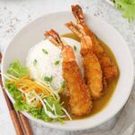 A white bowl containing rice with prawn katsu, curry sauce, and salad.