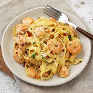 A white plate containing pasta with salmon and prawns with creamy sauce.