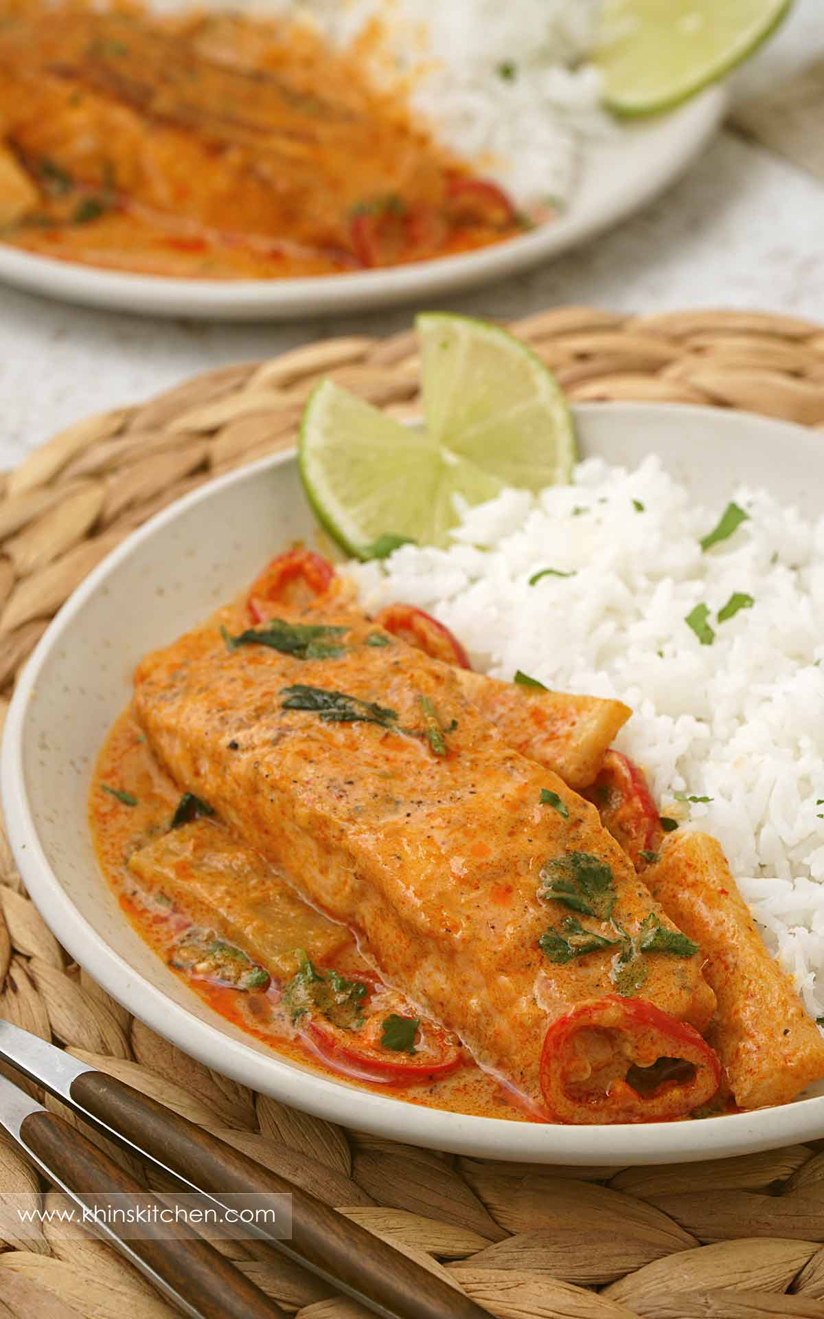 A grey plate containing salmon curry in creamy sauce, sliced bamboo shoots, sliced chilies and white rice on the side.