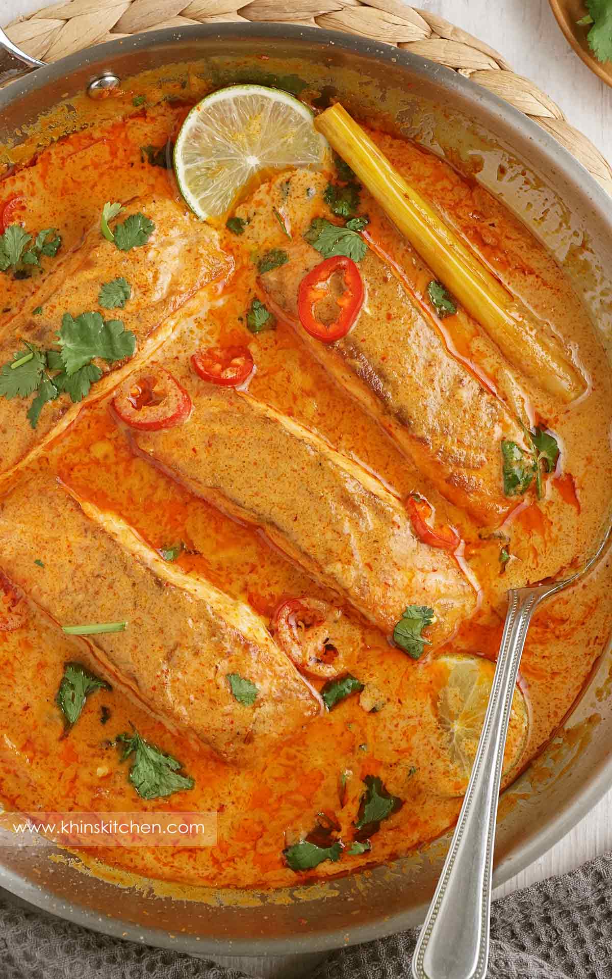 A steel pan containing salmon fillets with cream Thai red curry sauce, coriander and red chilli slices.