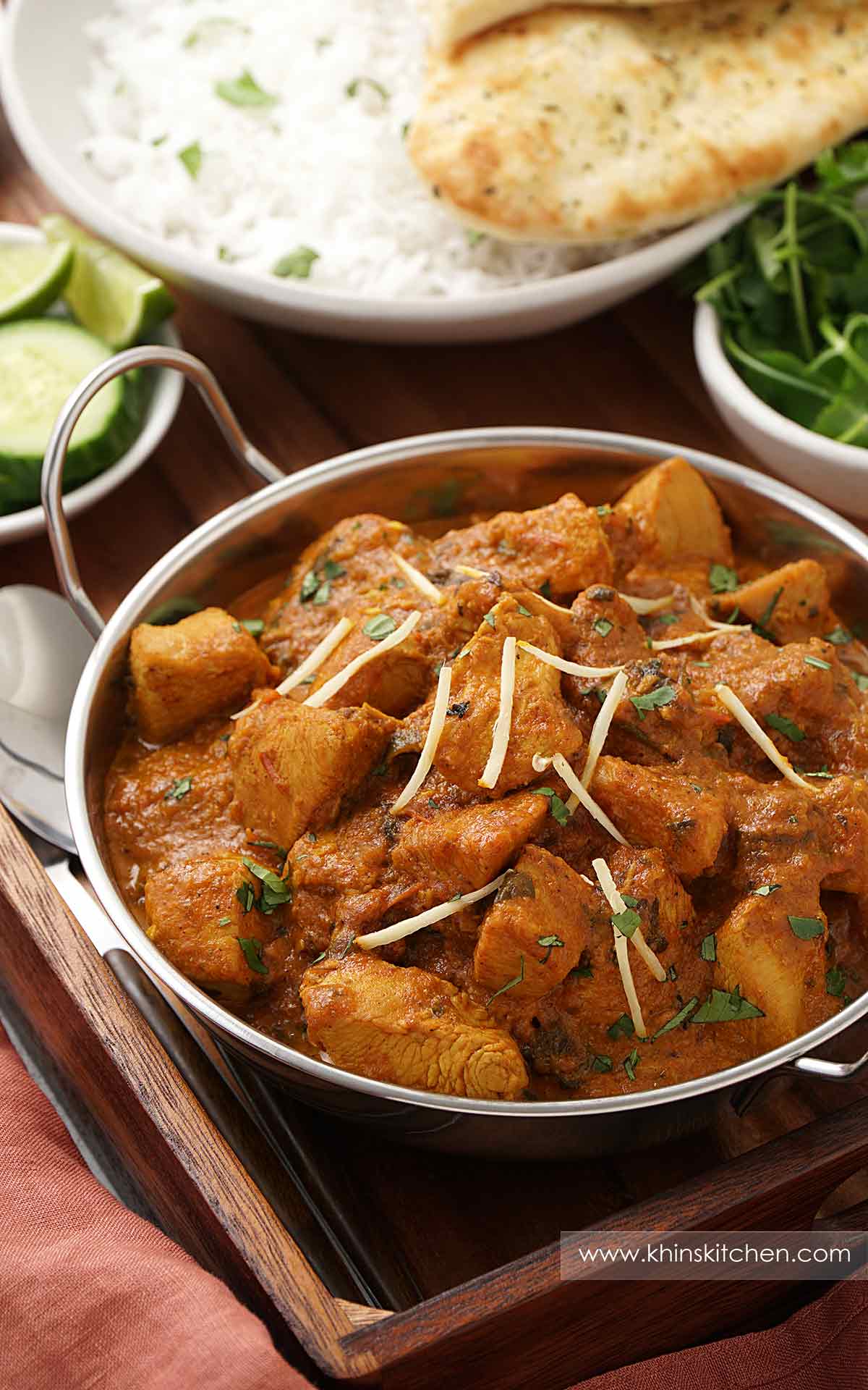 A metal serving bowl containing, chicken curry, garnish with ginger strips and coriander.