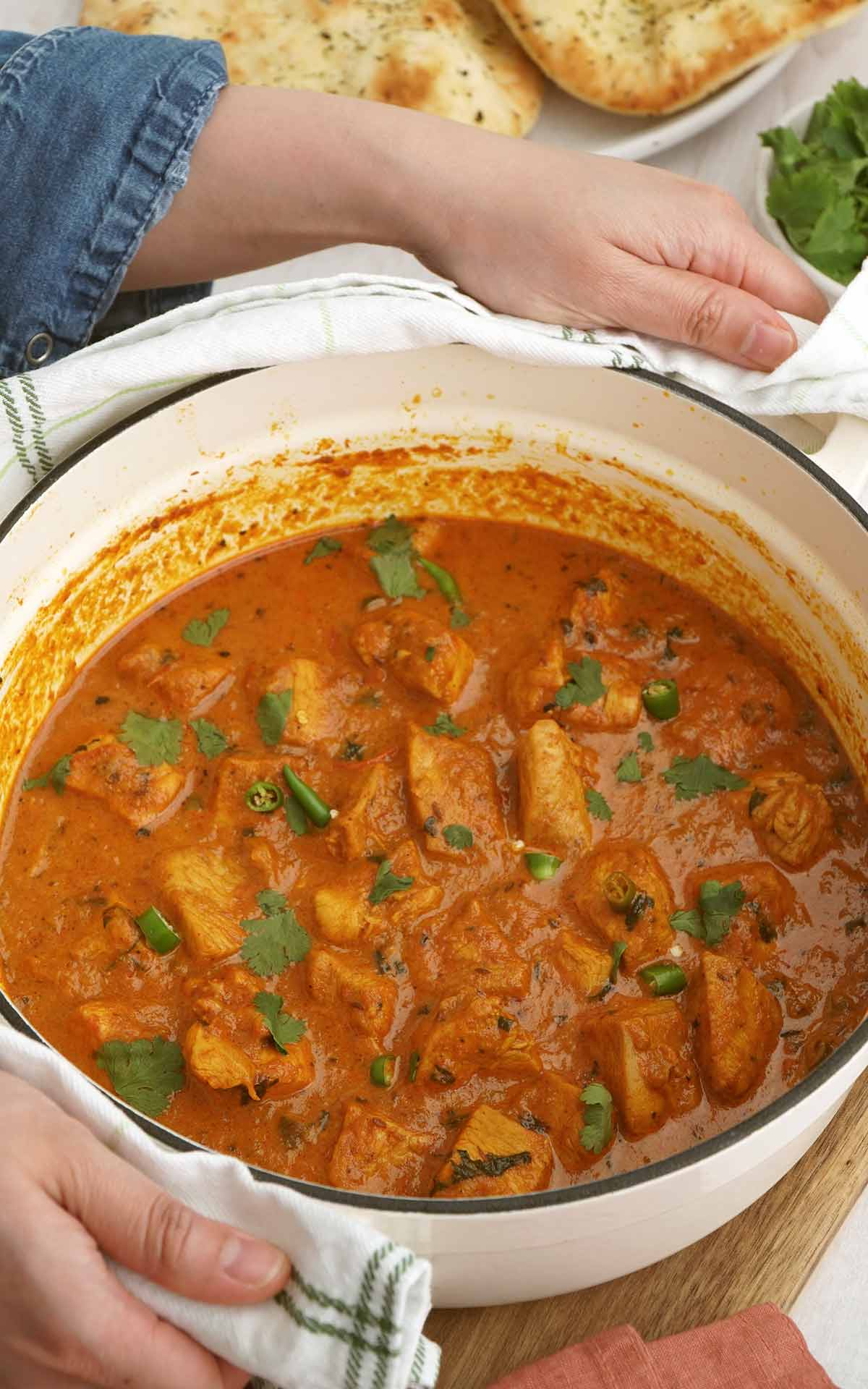 White cast-ion pot containing chicken handi,, holding with two hands. 