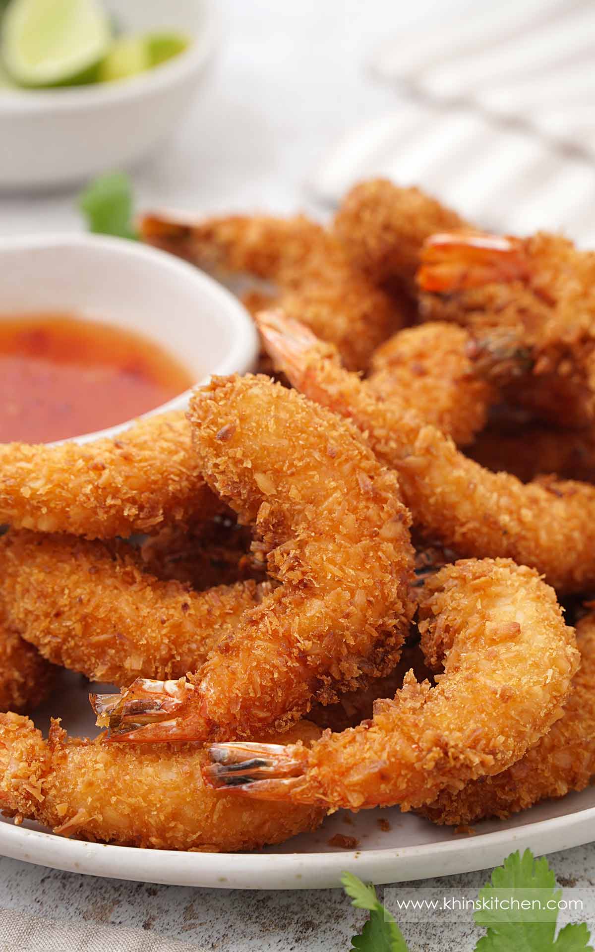 A white plate containing, fried crispy prawn with sweet chilli dipping sauce on the side.