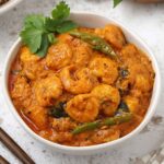 A white bowl containing creamy prawn curry with coconut milk, garnished with green chillies and coriander.