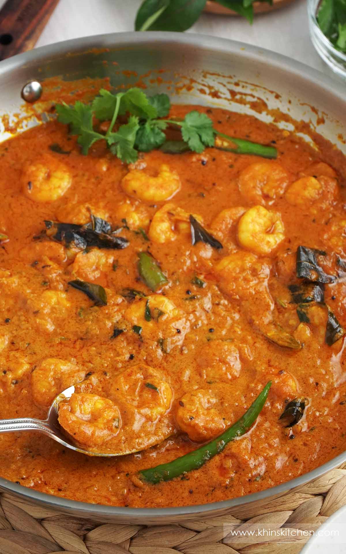 A steel pan containing prawn curry with coconut milk with coriander, curry leaves, green chillies.