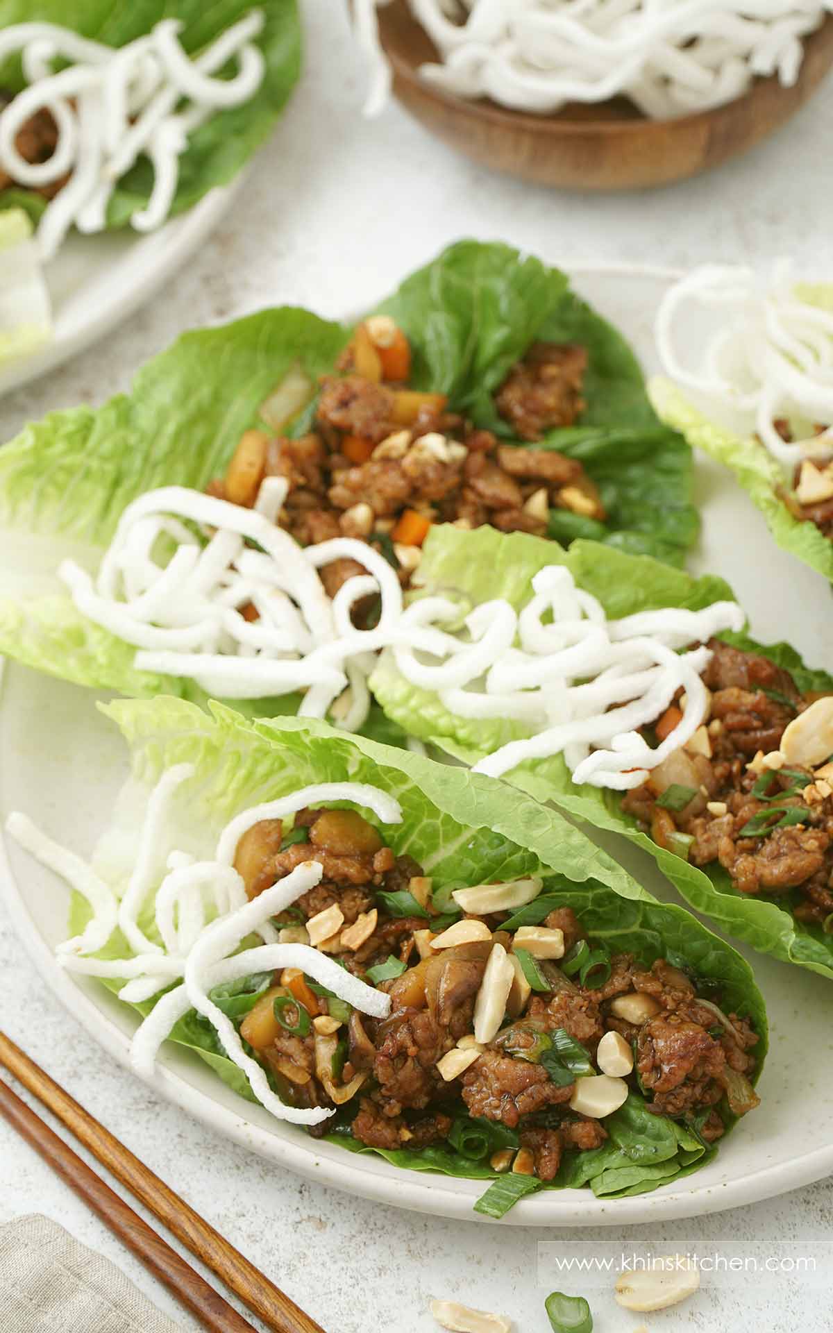 A white plate containing lettuce with chicken mince, vegetables, peanuts and fried rice stick.