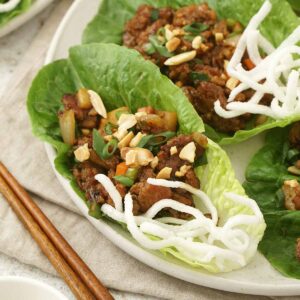 A white plate containing lettuce cup containing Chinese yuk sung with peanuts and fried rice crisp.