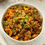 A white bowl containing fried rice with beef, egg, carrot, and spring onions.