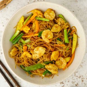 A white bowl containing, Singapore-style stir fried rice vermicelli noodles with prawns, chicken, and vegetables.
