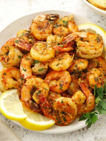 A grey plate containing pan-fried prawns with garlic butter sauce, garnished with parsley and lemon wedges.
