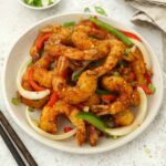 A white plate containing fried coated king prawns with vegetables and salt and pepper seasonings.