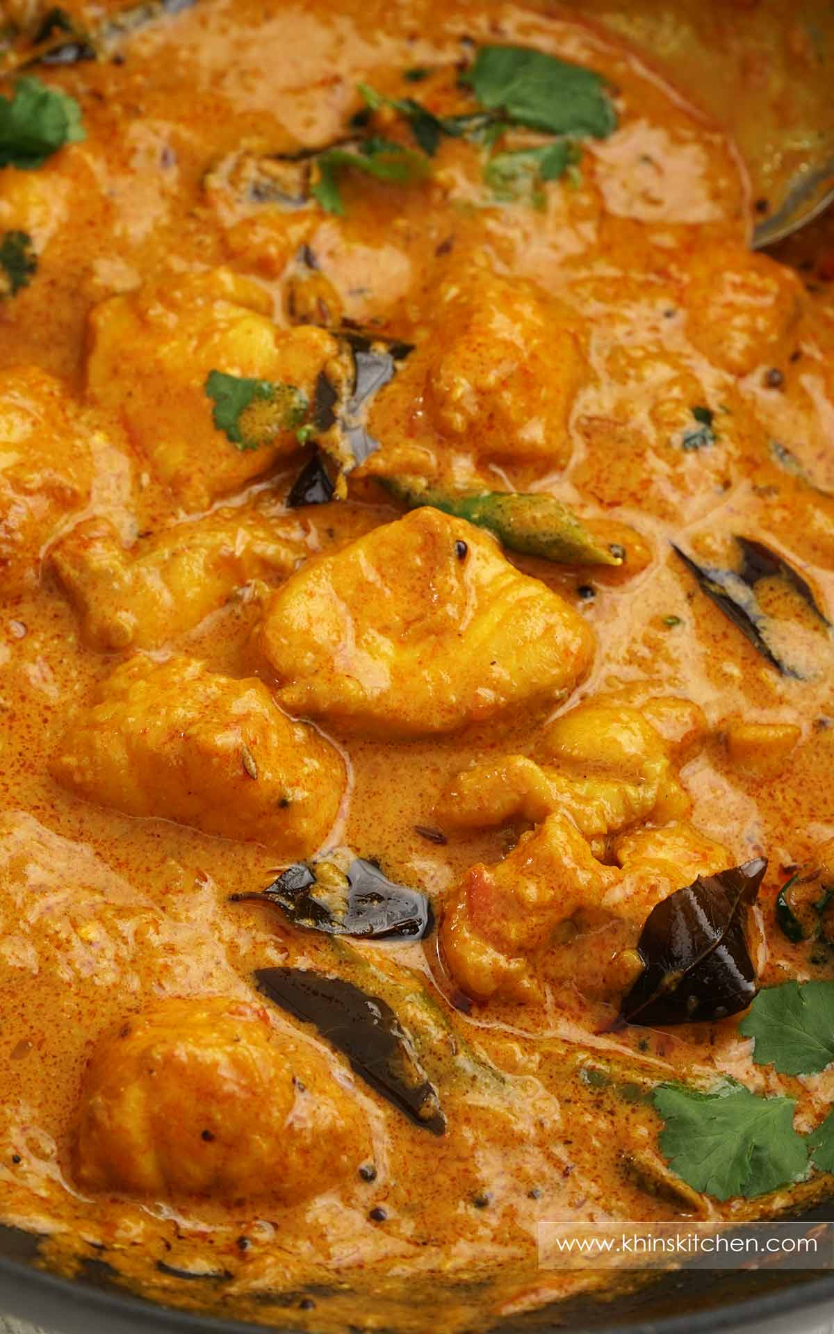 A black pan containing monkfish cooked in creamy curry sauce with green chillies, coriander, and curry leaves. 