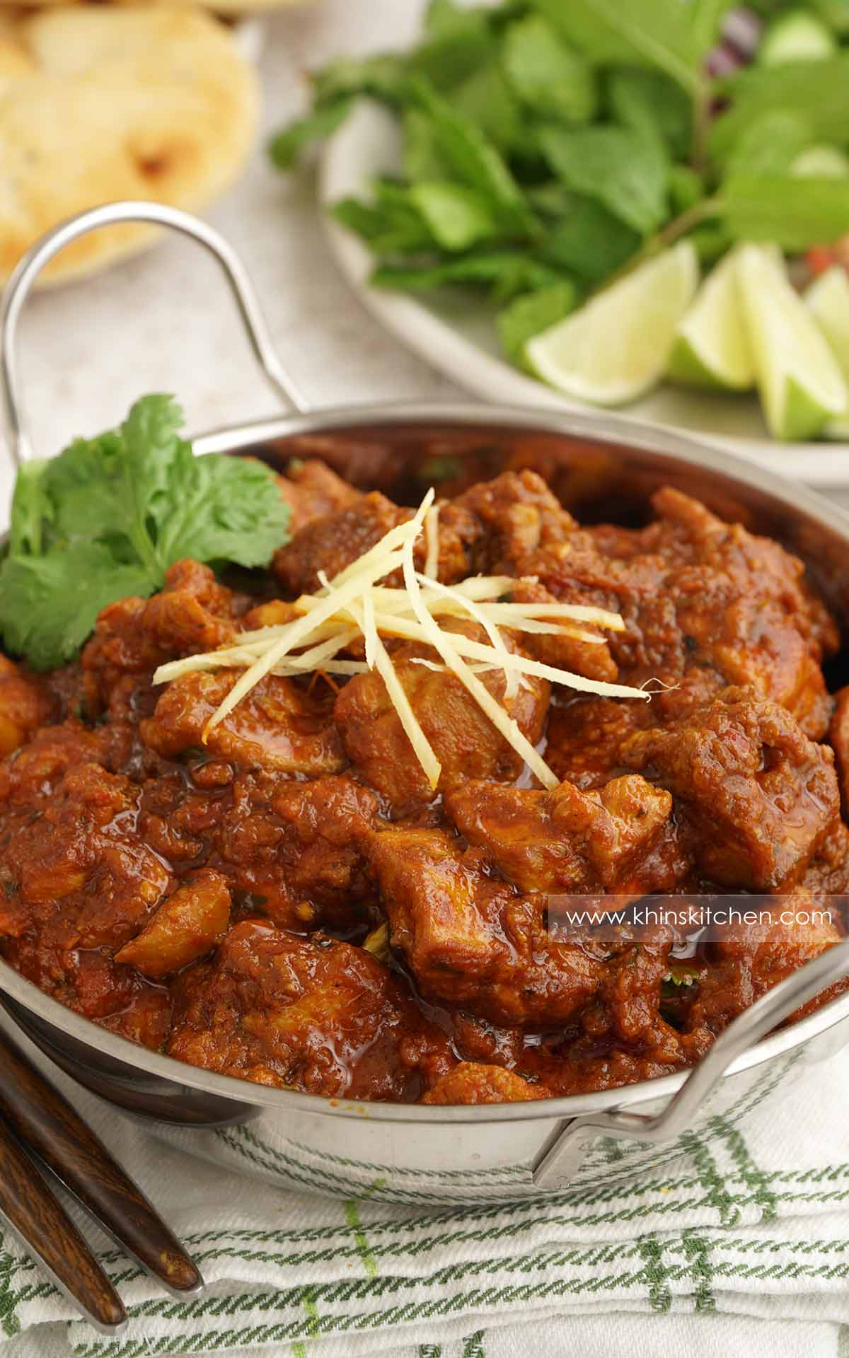 A metal serving bowl containing chicken curry, garnished with ginger strips and coriander. 