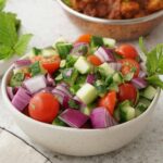 A white bowl containing, Indian style salad with small dices of onions, tomatoes, cucumber, and coriander leaves.
