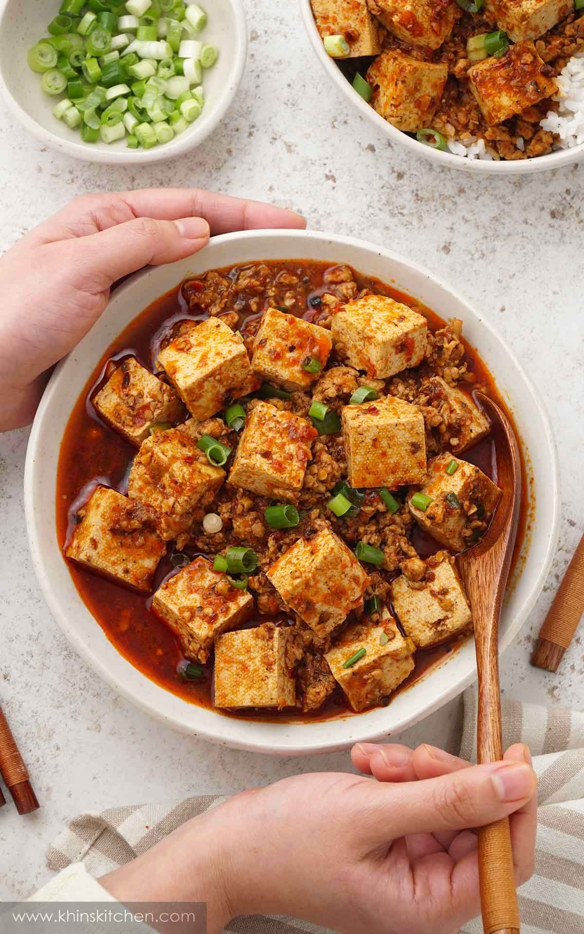 A white bowl containing Sichuan tofu dish with minced meat, spring onions, and spicy red mapo sauce. 