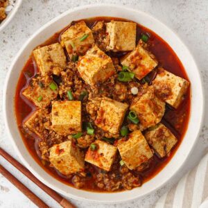 A white bowl containing, Sichuan Chinese tofu dish in red spicy mapo sauce.