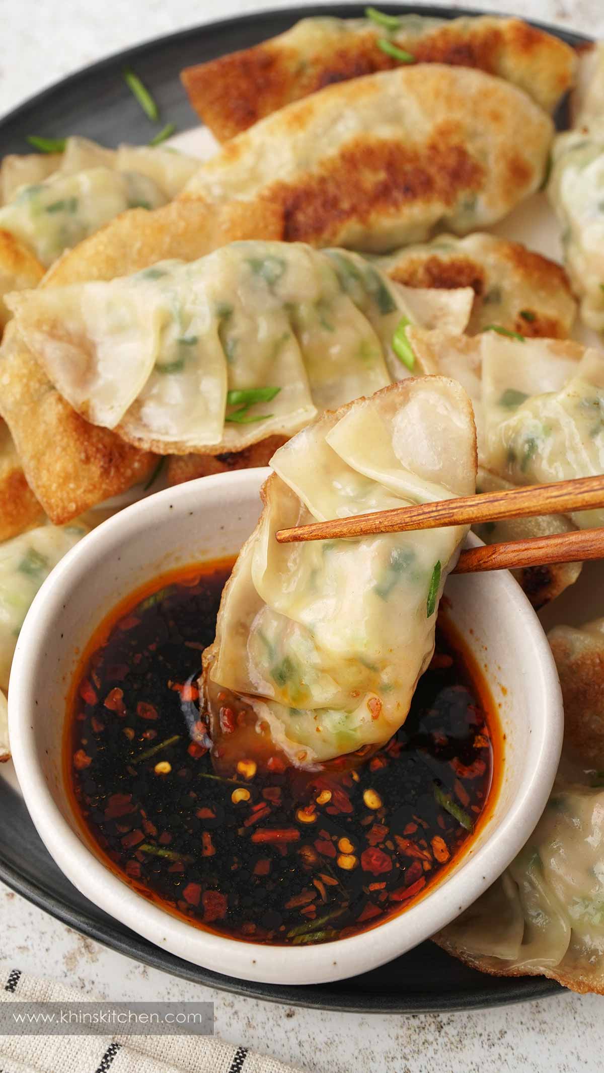 An image showing a pair of chopsticks holding Japanese pan-fried prawn dumplings, dipped in the sauce.