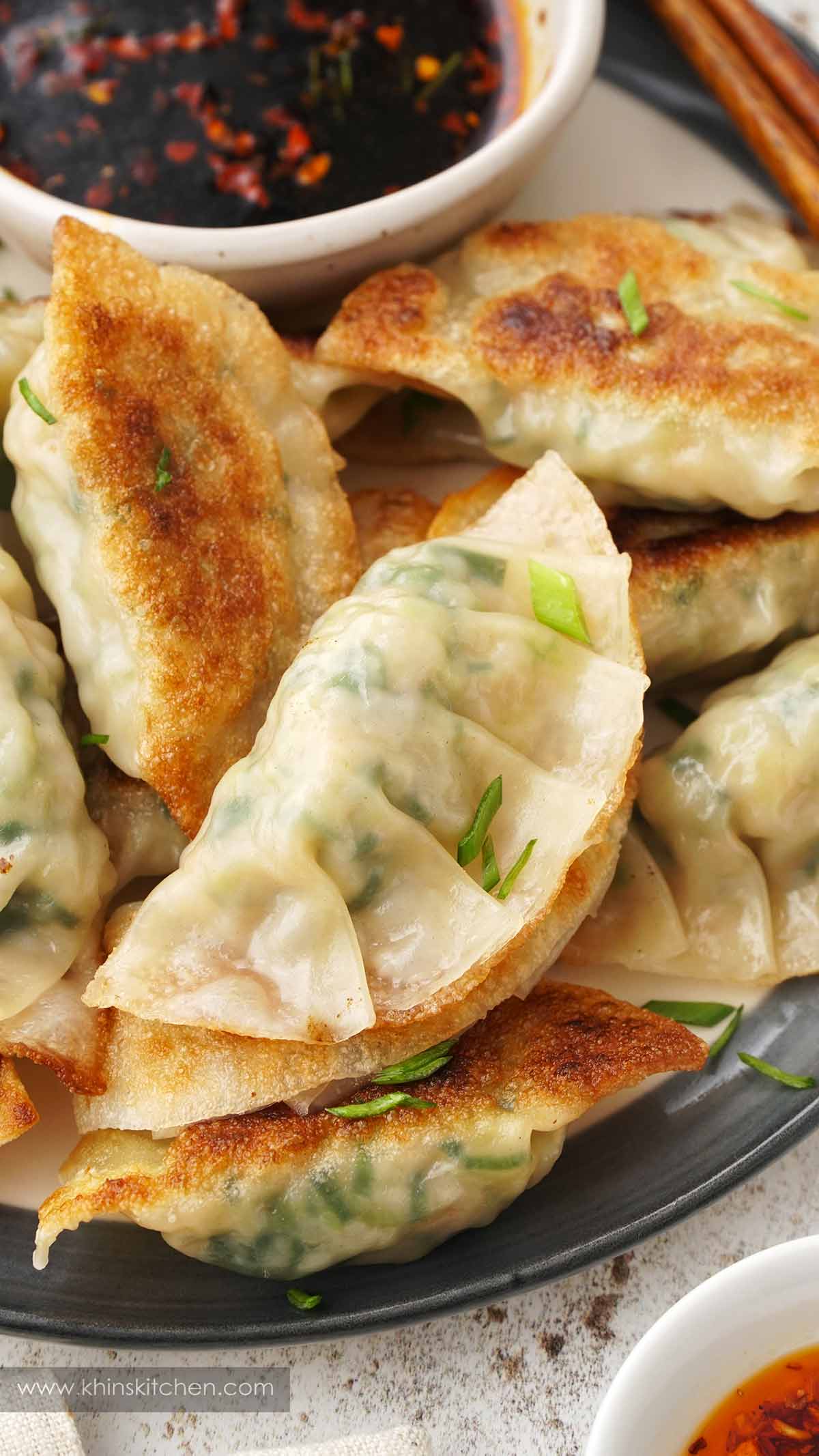 A grey plate containing pan-fried Japanese prawn gyoza dumplings with chives and dipping sauce.  