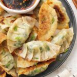 A grey plate containing, pan-fried prawn gyoza with dipping sauce on the side.