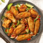 A grey plate containing, crispy fried golden colour chicken wings with vegetables.