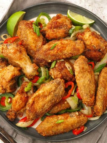 A grey plate containing, crispy fried golden colour chicken wings with vegetables.