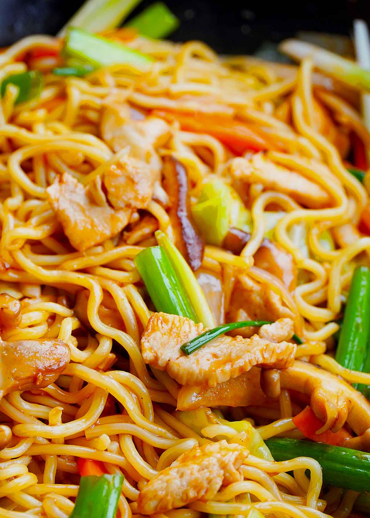 A black wok containing, stir fried Japanese noodles with chicken slices and vegetables.