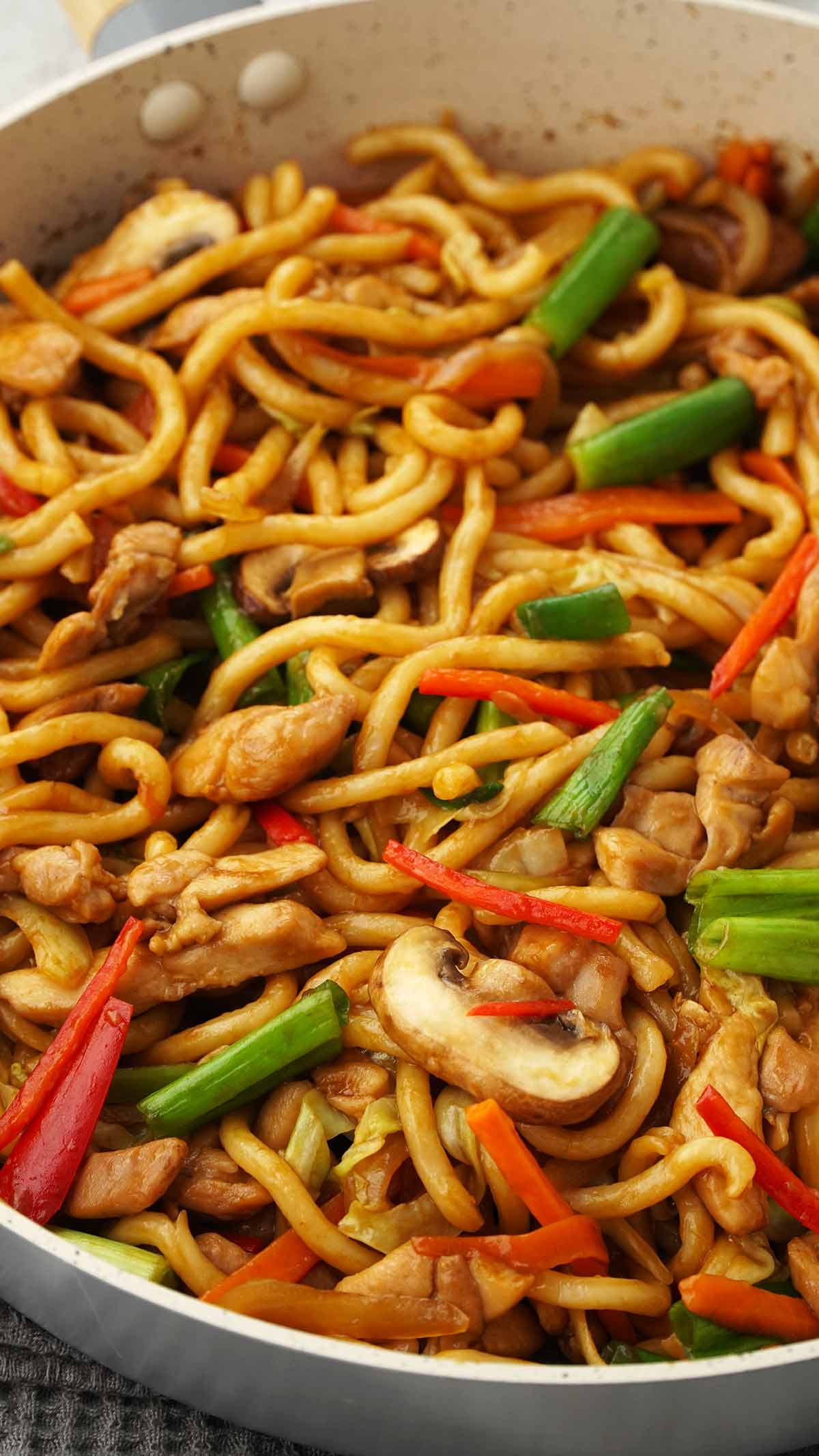 A white pan containing stir fried udon with chicken and colourful vegetables. 