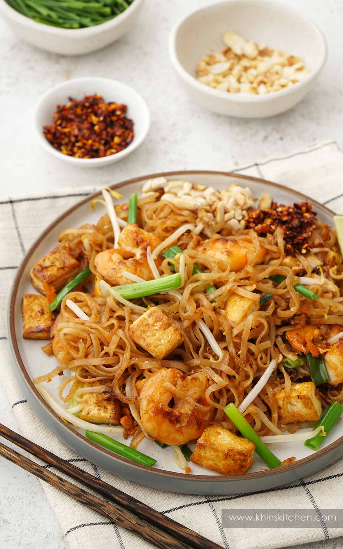 A white bowl containing Thai style rice noodles stir fry with prawns, bean sprouts, green onions, chilli flakes and crushed peanuts. 