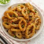 A white plate containing crispy coated squids with minced garlic, and chilli peppers.
