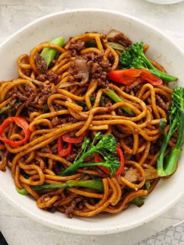 A white bowl containing fried noodles, minced beef, broccoli, and red chillies.