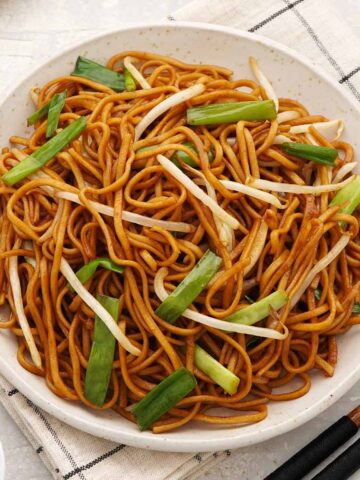 A white plate containing, fried brown chow mein noodles with bean sprouts and green onions.