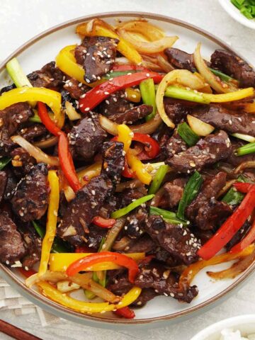 A white plate containing, stir fry steak with bell peppers, onions, and spring onions.