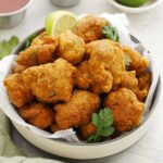 A white bowl containing, Indian restaurant-style crispy fried battered chicken pieces with dipping sauces on the side.