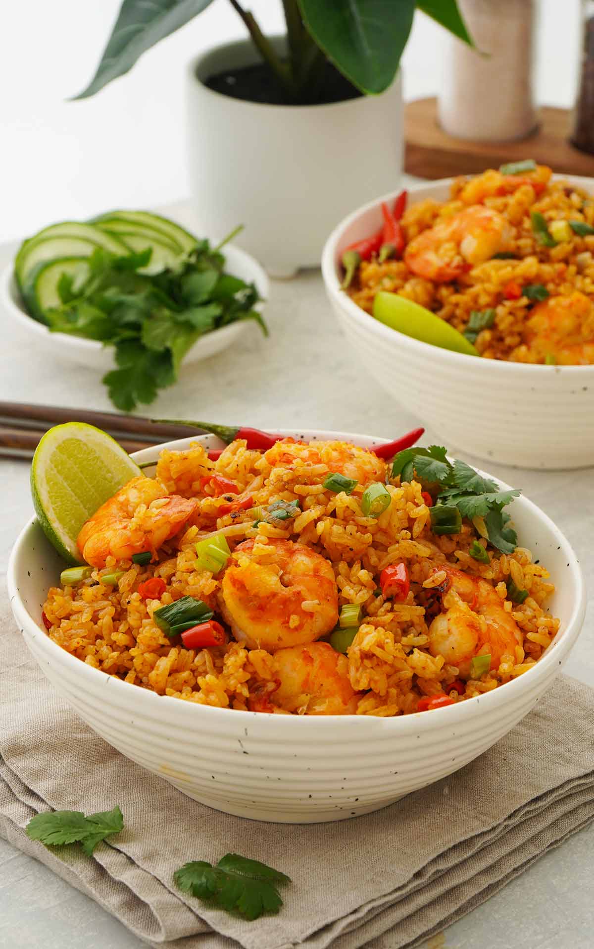 A white bowl containing spicy fried rice with Thai Tom Yum sauce, prawns, and lime wedges. 