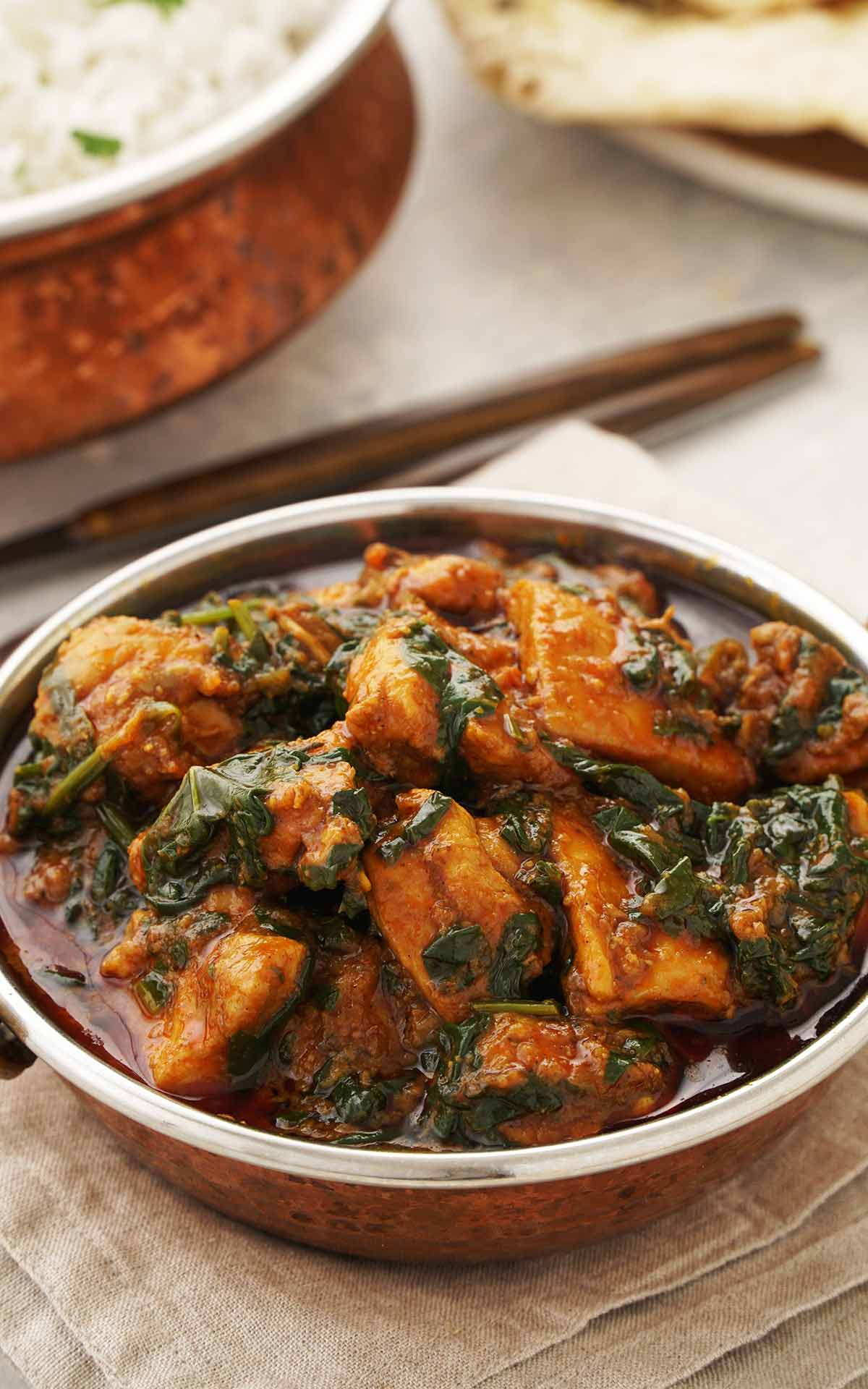 A metal serving bowl containing chicken curry with spinach. 