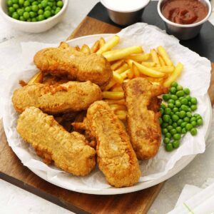 A white plate containing fried sausages with green peas, and potato chips.