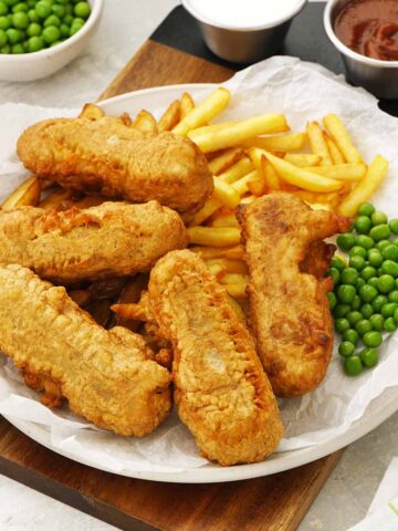 A white plate containing fried sausages with green peas, and potato chips.