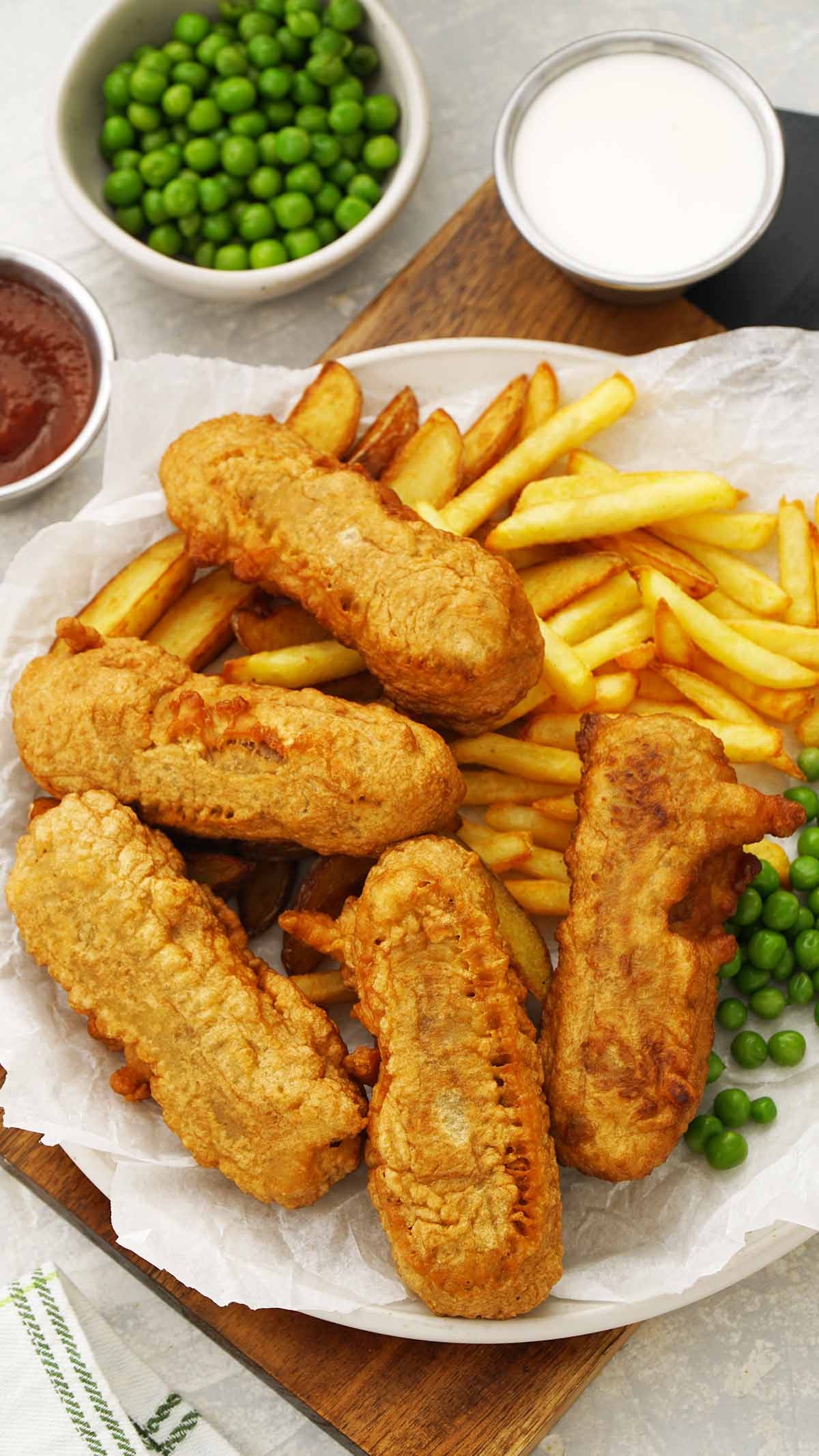 A white plate containing fried battered sausages with fries and peas. 