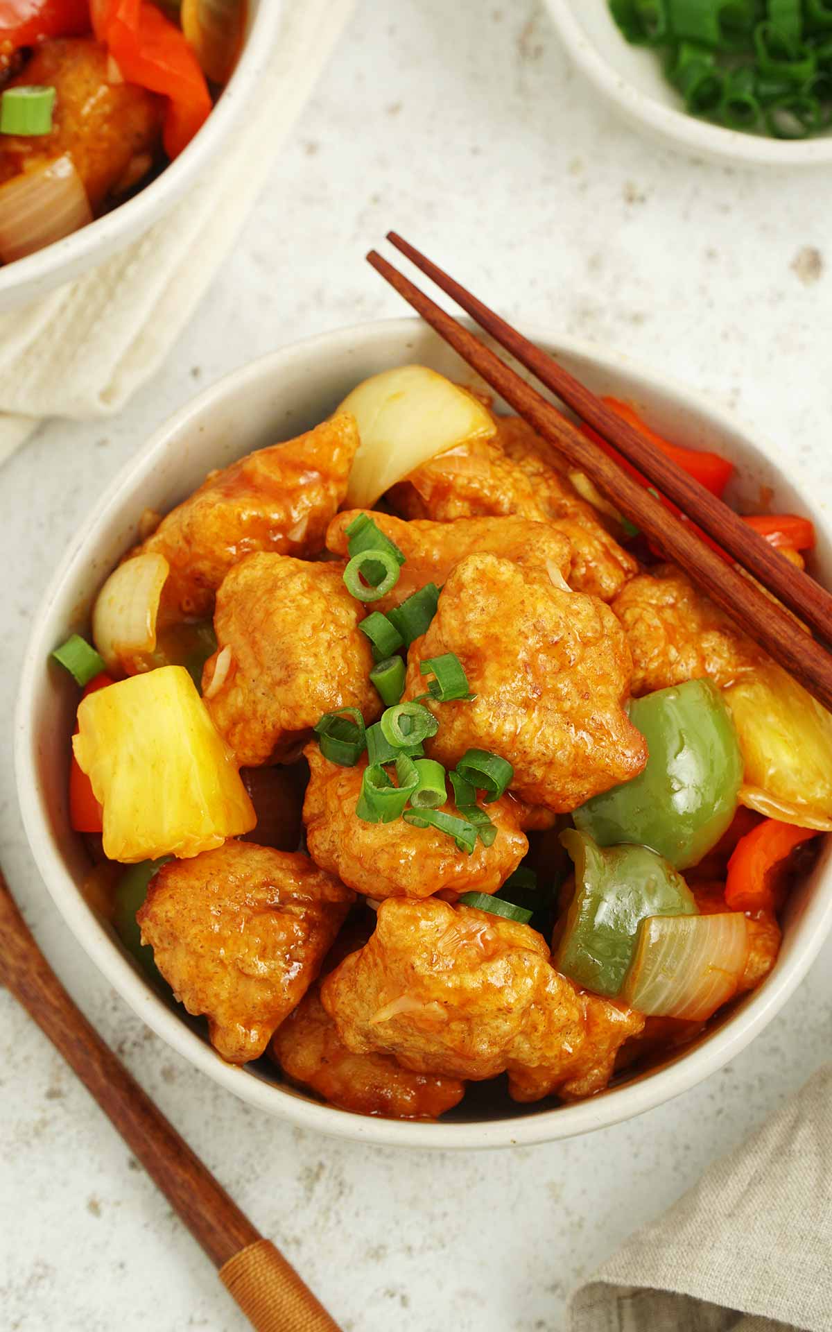 A white bowl containing, fried coated fish pieces with vegetables and sweet and sour sauce. 