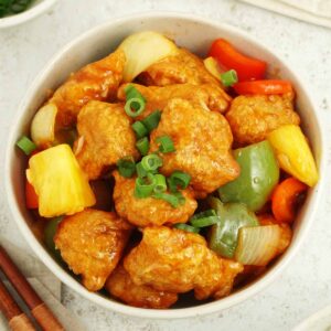 A white bowl containing fried fish with bell peppers, pineapple, onions, and sweet and sour sauce.
