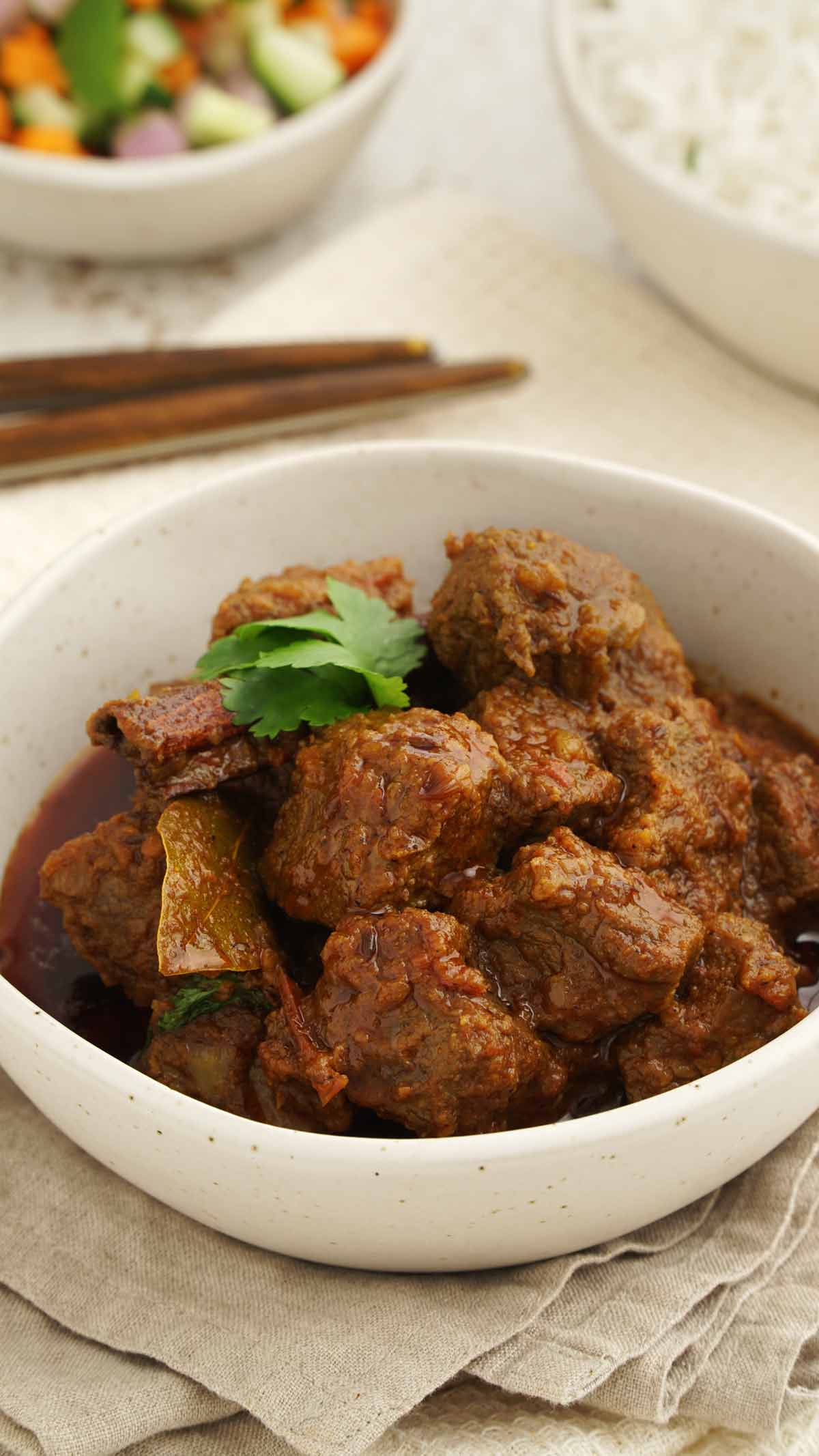 A white serving bowl containing beef chunks cooked in curry sauce. 