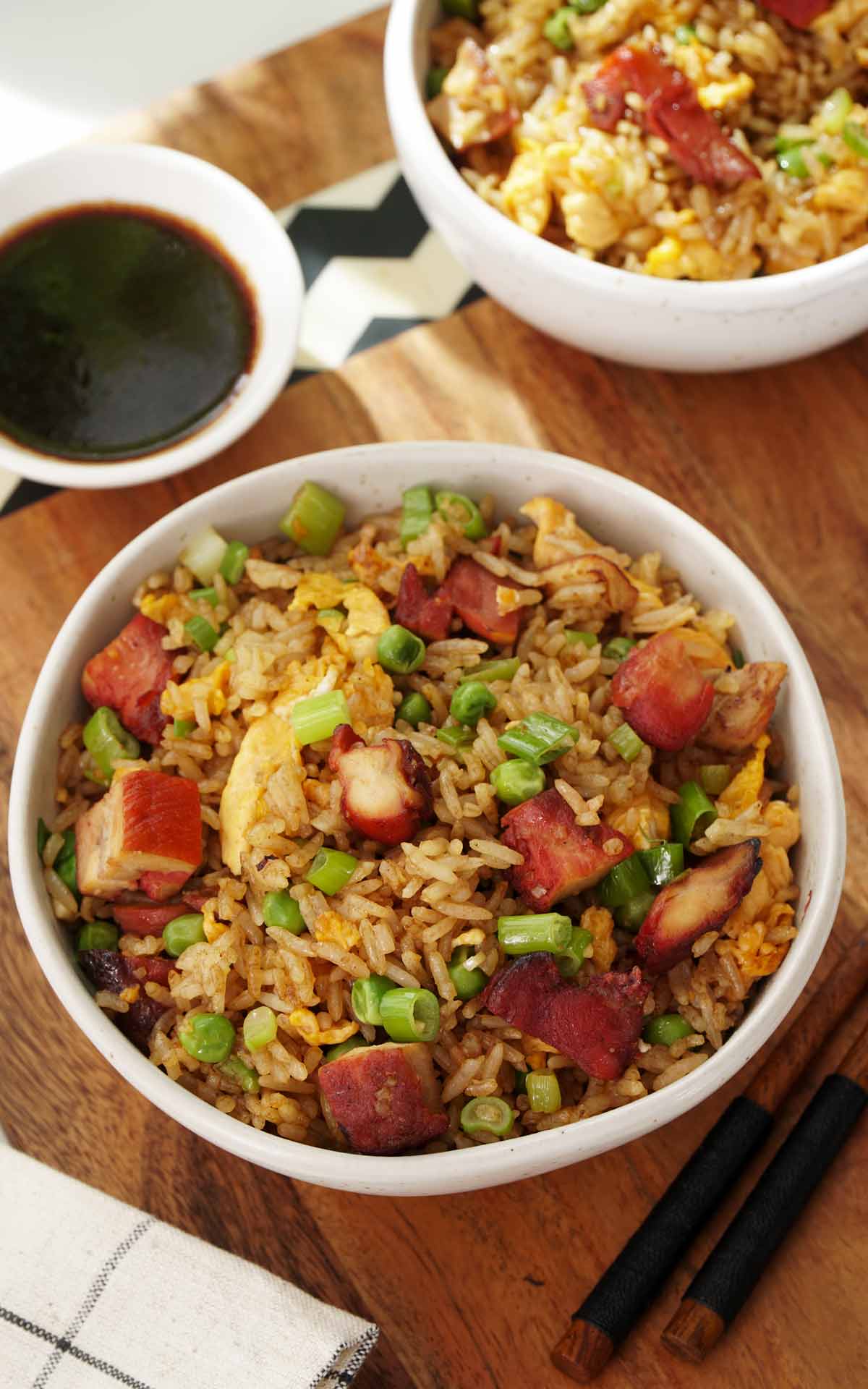 A white bowl containing Chinese style fried rice with char siu, egg, and peas. 